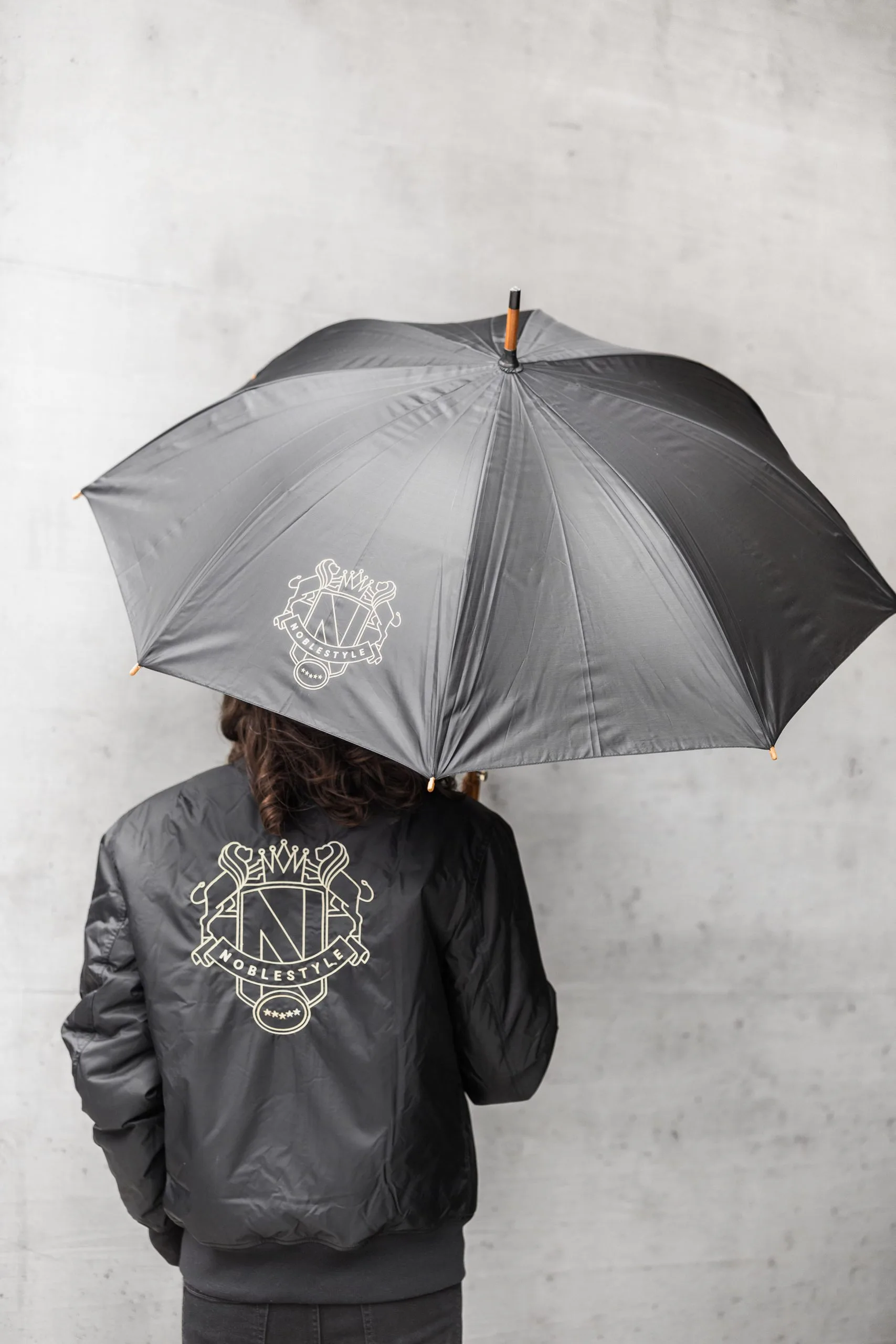 Noblestyle-Markenauftritt auf einem grauen Regenschirm und einer Jacke.